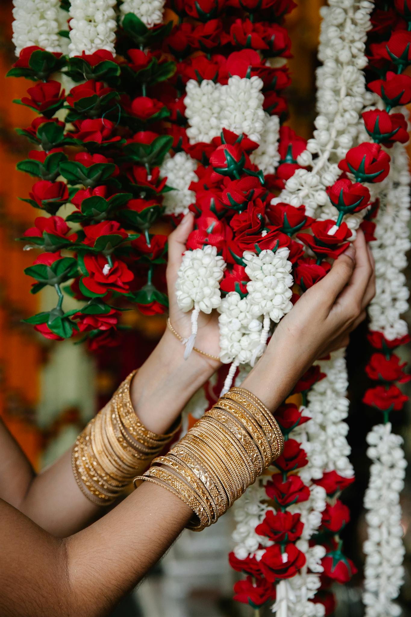 Close-up of hands arranging vibrant floral garlands wearing elegant gold bangles.